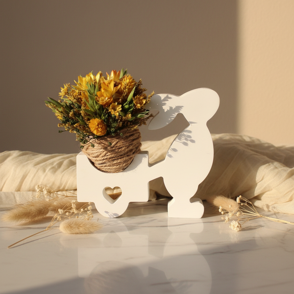 Vaso decorativo em formato de coelho puxando carrinho com flores secas sobre superfície clara, peça de decoração delicada