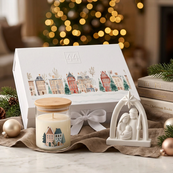 Coffret Premium com vela de tampa de bambu, presépio branco e caixa com laço, com árvore de Natal ao fundo.