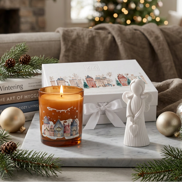 Coffret Âmbar com vela acesa, anjo de cerâmica perfumada e caixa de oferta, sobre mármore em ambiente natalício.