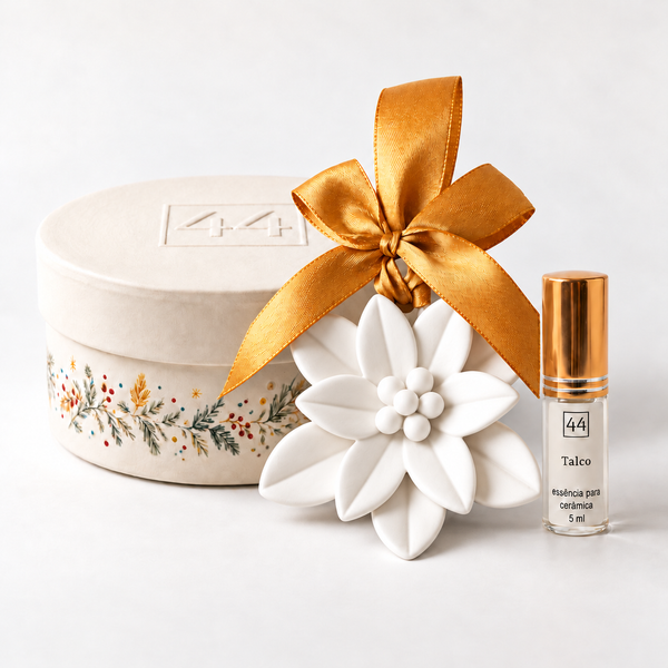 Estrela de Natal branca de cerâmica perfumada com laço dourado, essência de talco de 5 ml e caixa redonda da 44, sobre fundo claro.