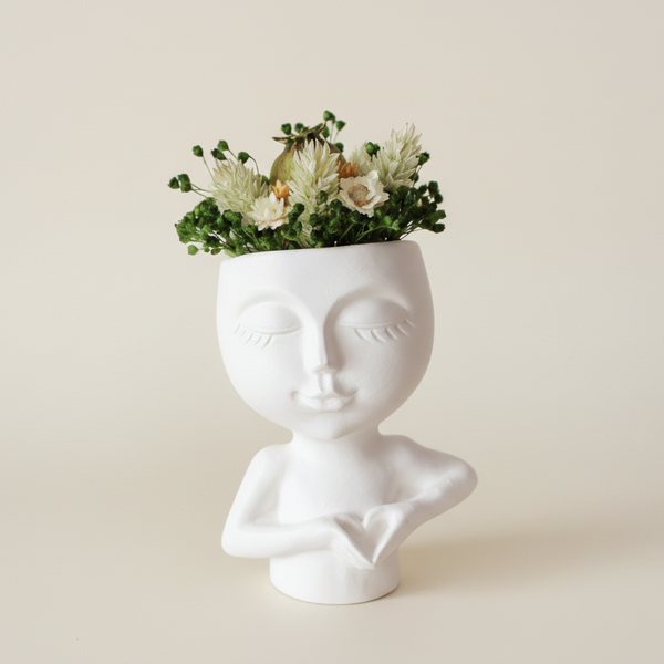 Jarra decorativa branca com rosto estilizado e mãos formando coração com flores secas.