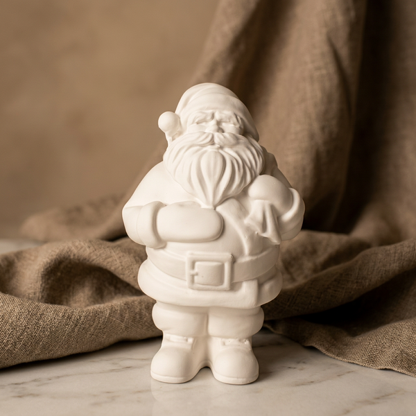 Pai Natal branco de cerâmica perfumada, com gorro e cinto com fivela, sobre mármore junto a tecido bege.