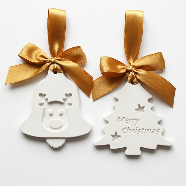 Sino com rena e pinheiro com inscrição Merry Christmas, em cerâmica branca com laços dourados, sobre fundo claro.