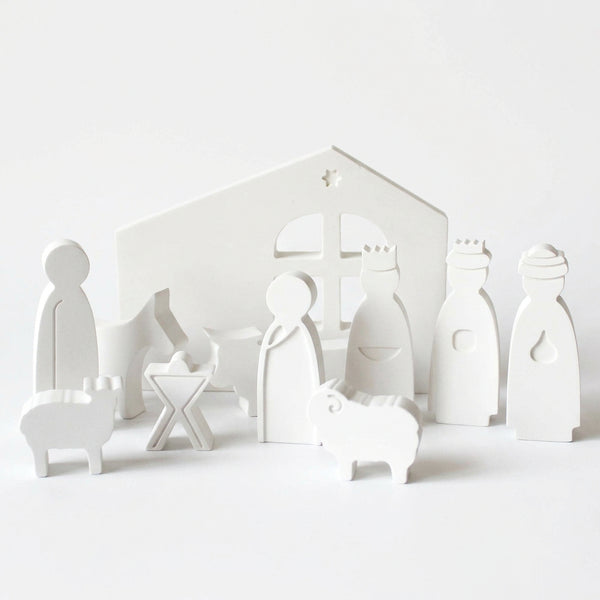 Conjunto de presépio branco com cabana de janela recortada, figuras e animais, sobre fundo claro.