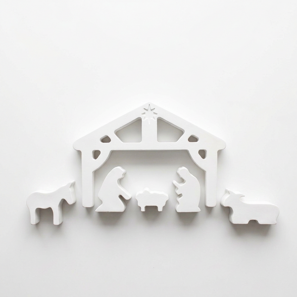 Presépio branco com cabana aberta, figuras da Sagrada Família e animais, sobre fundo claro.