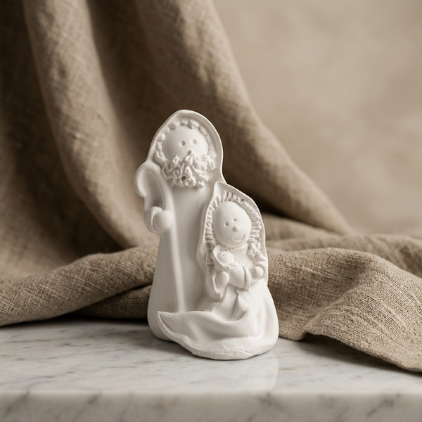 Mini presépio de cerâmica perfumada branca com a Sagrada Família, sobre mármore junto a tecido bege.
