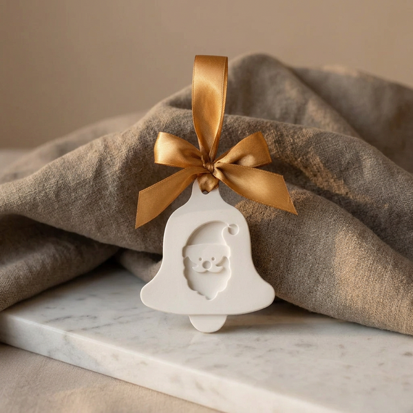Sino de cerâmica perfumada branca com Pai Natal em relevo e laço dourado, junto a tecido bege.