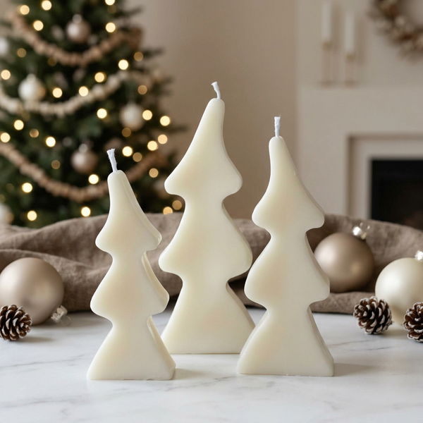 Trio de velas decorativas em forma de pinheiros estilizados, em três tamanhos, junto a uma árvore de Natal.