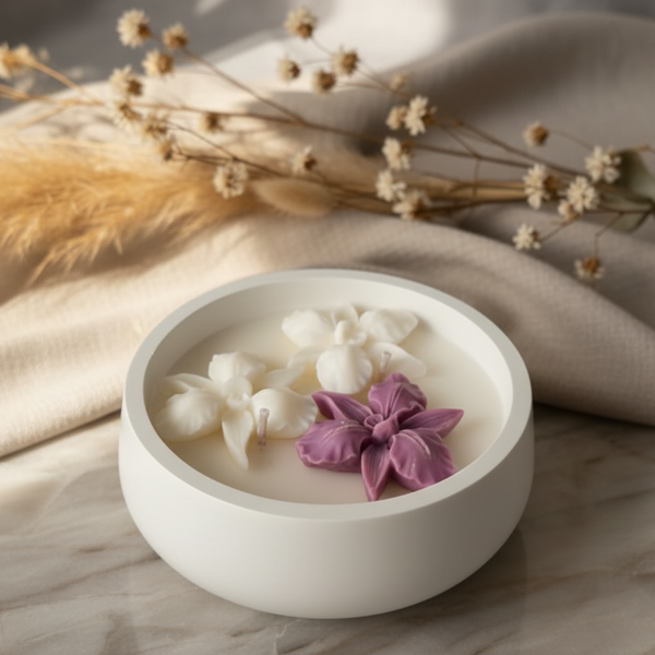 Vela artesanal em mini taça de cerâmica branca com orquídeas de cera decorativas.