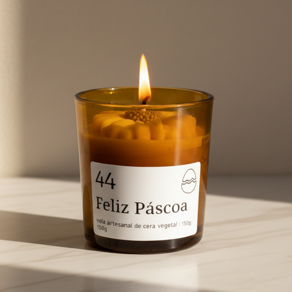 Vela aromática artesanal de Páscoa em copo de vidro âmbar com decoração floral e rótulo “Feliz Páscoa”.