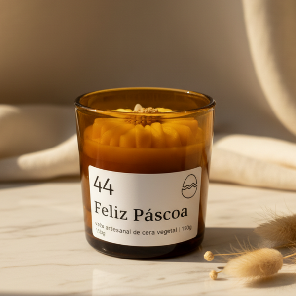 Vela aromática artesanal de Páscoa em copo de vidro âmbar com decoração floral e rótulo “Feliz Páscoa”.