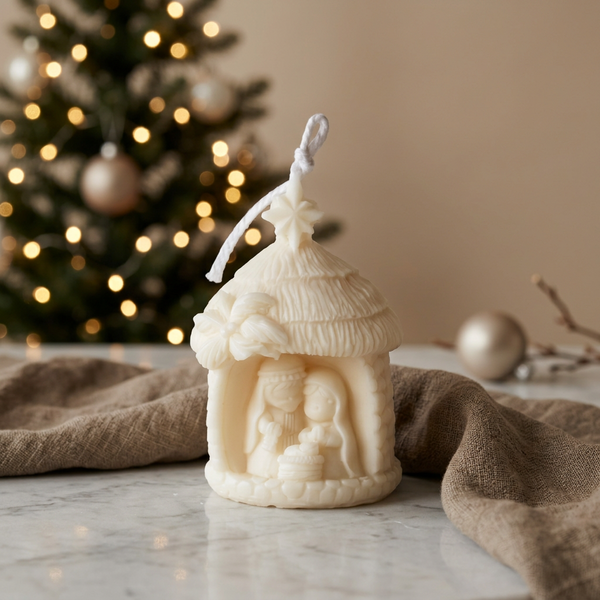 Vela decorativa Presépio em cera de soja, com telhado texturado e estrela no topo, junto a uma árvore de Natal.