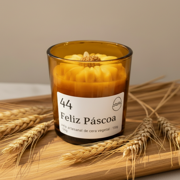Vela aromática artesanal de Páscoa em copo de vidro âmbar com decoração floral e rótulo “Feliz Páscoa”.