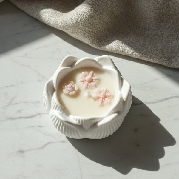 Vela artesanal em taça de cerâmica branca com formato de flor de lótus.
