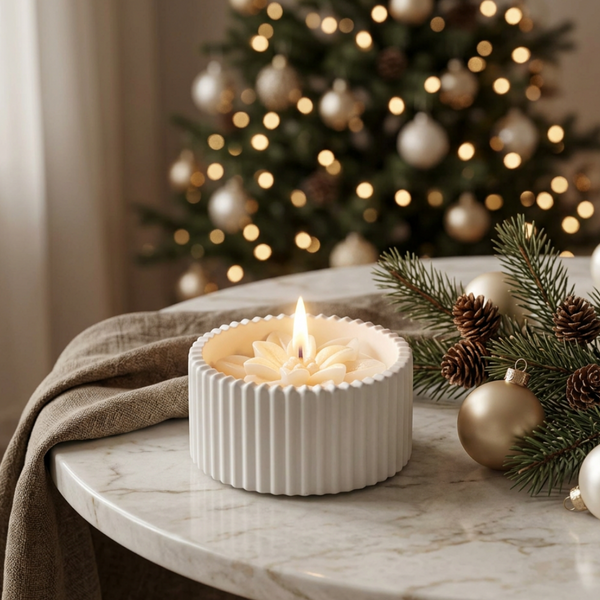 Vela de Natal acesa em pote de cerâmica branca raiada, com Estrela de Natal em cera, junto a ramos e bolas douradas.