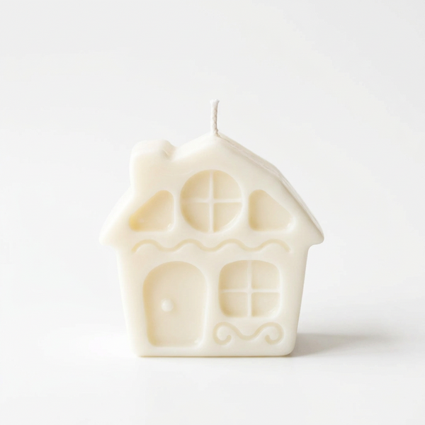Vela decorativa em forma de casinha, em cera de soja de tom claro, sobre fundo branco.