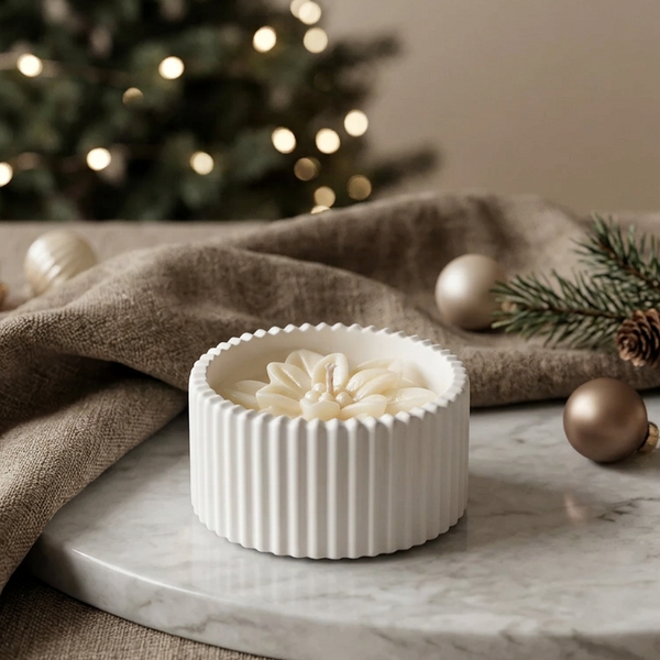Vela em pote de cerâmica branca raiada com Estrela de Natal em cera, junto a uma árvore de Natal.