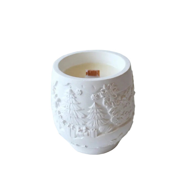 Vela de Natal em pote de cerâmica branca com árvores em relevo e pavio de madeira, sobre fundo branco.