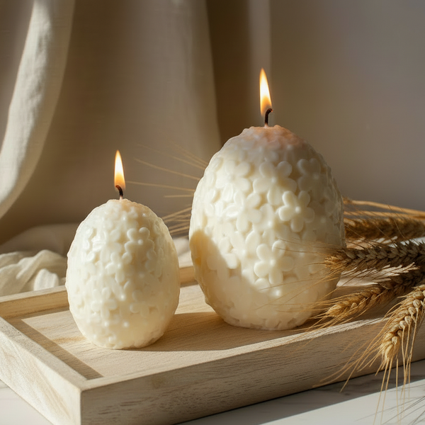 Velas decorativas de Páscoa em formato de ovo com flores em relevo sobre superfície de mármore.